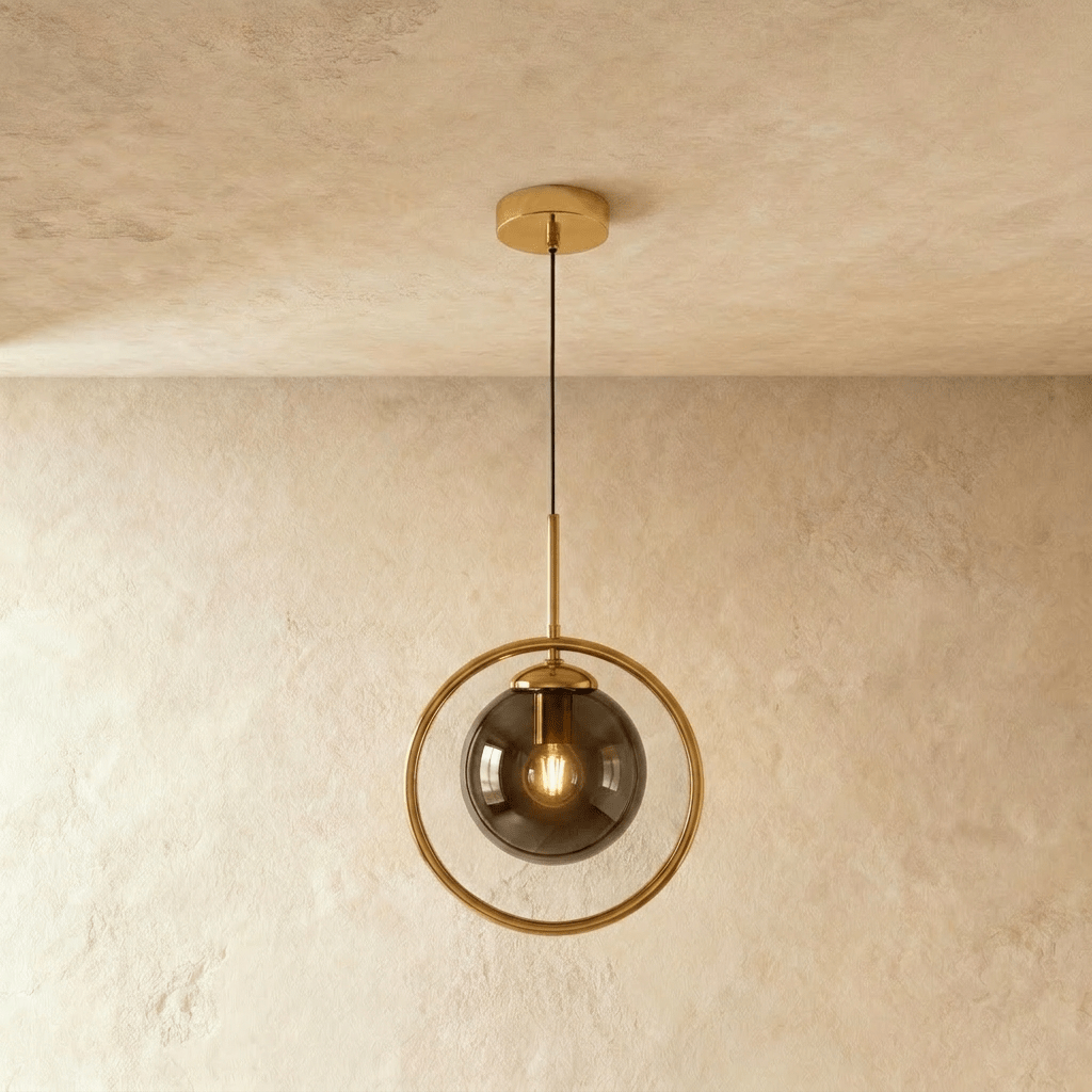 Clérachic gold ring pendant with a smoky ash glass globe and a filament bulb, hung on a thin cord in a studio