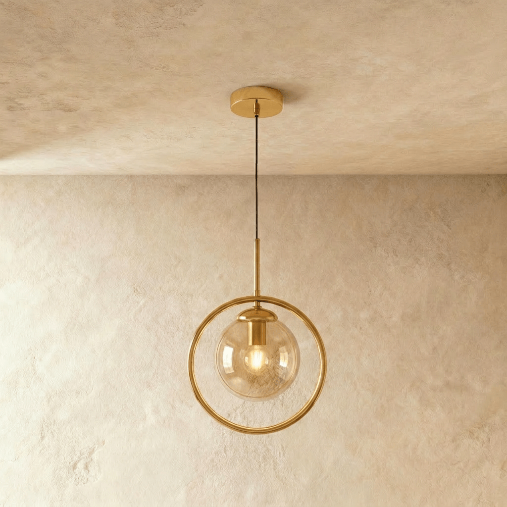 Clérachic gold ring pendant holding an amber glass globe with a filament bulb glowing, shown in a studio