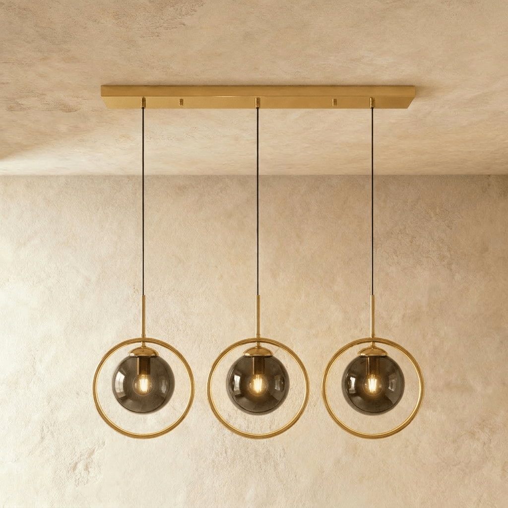Clérachic row of three gold ring pendants with smoky ash glass globes hung from one long gold ceiling bar in a studio