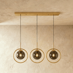 Clérachic row of three gold ring pendants with smoky ash glass globes hung from one long gold ceiling bar in a studio