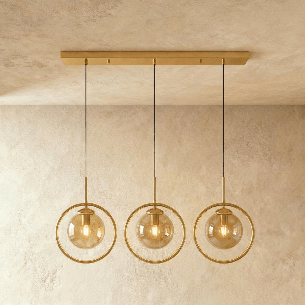 Clérachic three gold ring pendants with amber glass globes on a long brass ceiling bar, lit warm in a studio