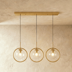 Clérachic three gold ring pendants with clear glass globes hung from a long gold ceiling bar, lit in a studio