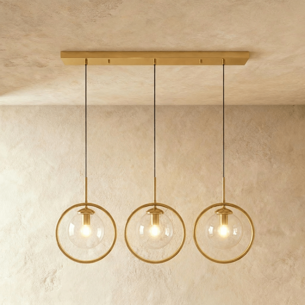 Clérachic three gold ring pendants with clear glass globes hung from a long gold ceiling bar, lit in a studio