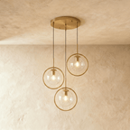 Clérachic cluster of three gold ring pendants with clear glass globes on a round gold canopy, in a studio
