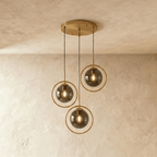 Clérachic cluster of three gold ring pendants with smoky ash glass globes at staggered heights from a round canopy in a studio