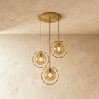 Clérachic cluster of three gold ring pendants with amber glass globes at staggered drops from a round canopy in a studio