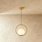 Clérachic gold ring pendant with a lit white opal glass globe set low in the ring, hung on a cord in a studio