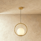 Clérachic larger gold ring pendant with a white opal glass globe resting in the lower ring, shown in a studio