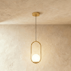 Clérachic gold oval ring pendant with a glowing white opal glass globe at the base of the frame, shown in a studio