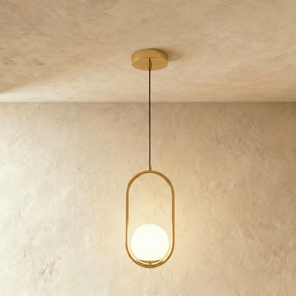 Clérachic taller gold oval ring pendant with a white opal glass globe at its base, hung on a cord in a studio