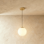 Clérachic gold pendant with a small white opal glass globe on a slim cord below a round gold canopy, shown in a studio