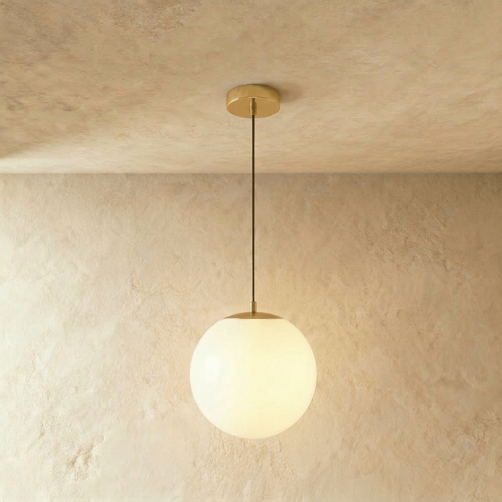 Clérachic gold pendant with a large white opal glass globe glowing on a slim cord below a round canopy, in a studio