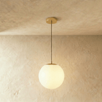 Clérachic gold pendant with a large white opal glass globe glowing on a slim cord below a round canopy, in a studio
