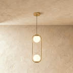 Clérachic tall gold oval frame pendant holding two white opal glass globes, one above the other, shown in a studio