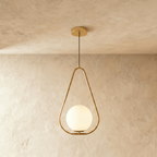Clérachic gold teardrop frame pendant with a white opal glass globe at its base, hung on a cord in a studio