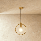 Clérachic gold ring pendant with a bare frosted bulb on a brass holder, hung from a round gold canopy in a studio