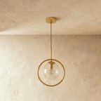 Clérachic gold ring pendant with a clear glass globe and a visible filament bulb on a slim rod, shown unlit in a studio