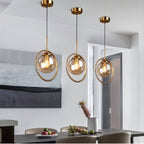 Clérachic three gold ring pendants with amber glass globes at different heights above a dark dining table in a room