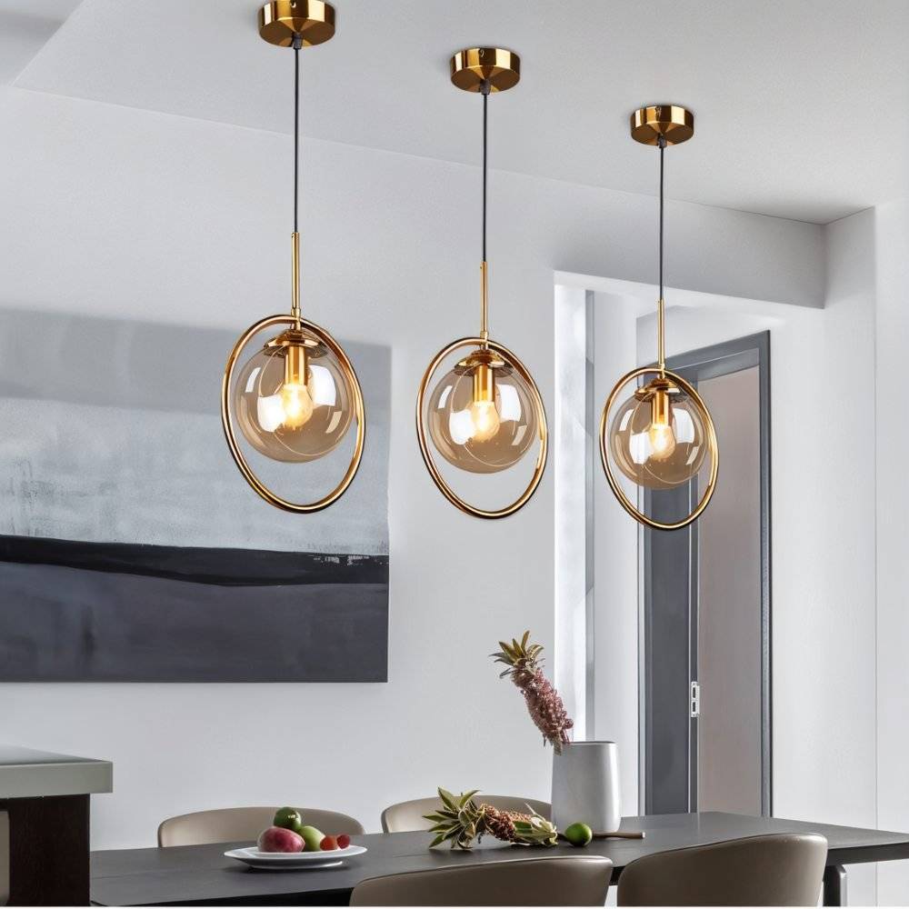 Clérachic three gold ring pendants with amber glass globes at different heights above a dark dining table in a room