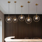 Clérachic five gold ring pendants with clear glass globes at varied heights in front of dark slatted panelling in a room