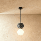 Clérachic two-globe pendant light with a black terrazzo sphere above a glowing opal glass globe on a slim black cord.