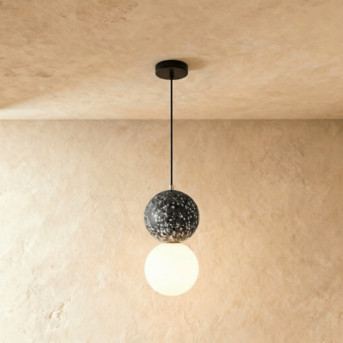 Clérachic two-globe pendant light with a black terrazzo sphere above a glowing opal glass globe on a slim black cord.