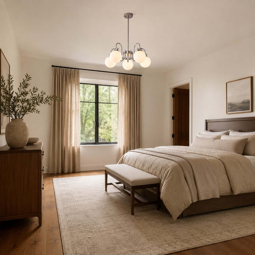 This Clérachic chandelier hangs in a calm bedroom with linen curtains, a wood-framed bed and an upholstered bench at its foot.