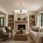 Glass globes on chrome arms hang before a fireplace in a living room with olive armchairs, a Clérachic chandelier.