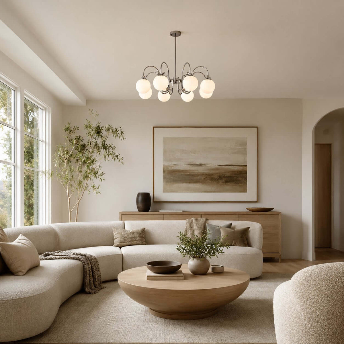 Above a curved cream sofa and a round wooden coffee table, this Clérachic chandelier glows in a bright living room.
