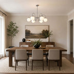Centred over a walnut dining table with grey chairs, this Clérachic chandelier sits under a framed landscape painting.