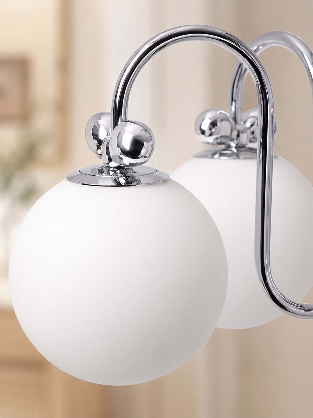 Close view of two frosted white glass globes and the curved chrome arms on this Clérachic chandelier.