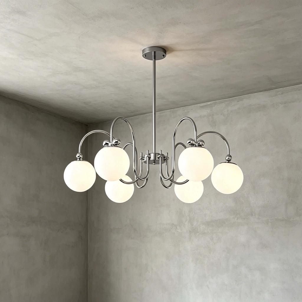 Six frosted globes on swooping chrome arms, this Clérachic chandelier hangs against a grey concrete-look wall and ceiling.