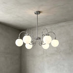 Six frosted globes on swooping chrome arms, this Clérachic chandelier hangs against a grey concrete-look wall and ceiling.