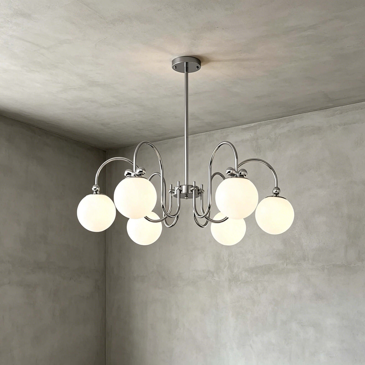 Six frosted globes on swooping chrome arms, this Clérachic chandelier hangs against a grey concrete-look wall and ceiling.
