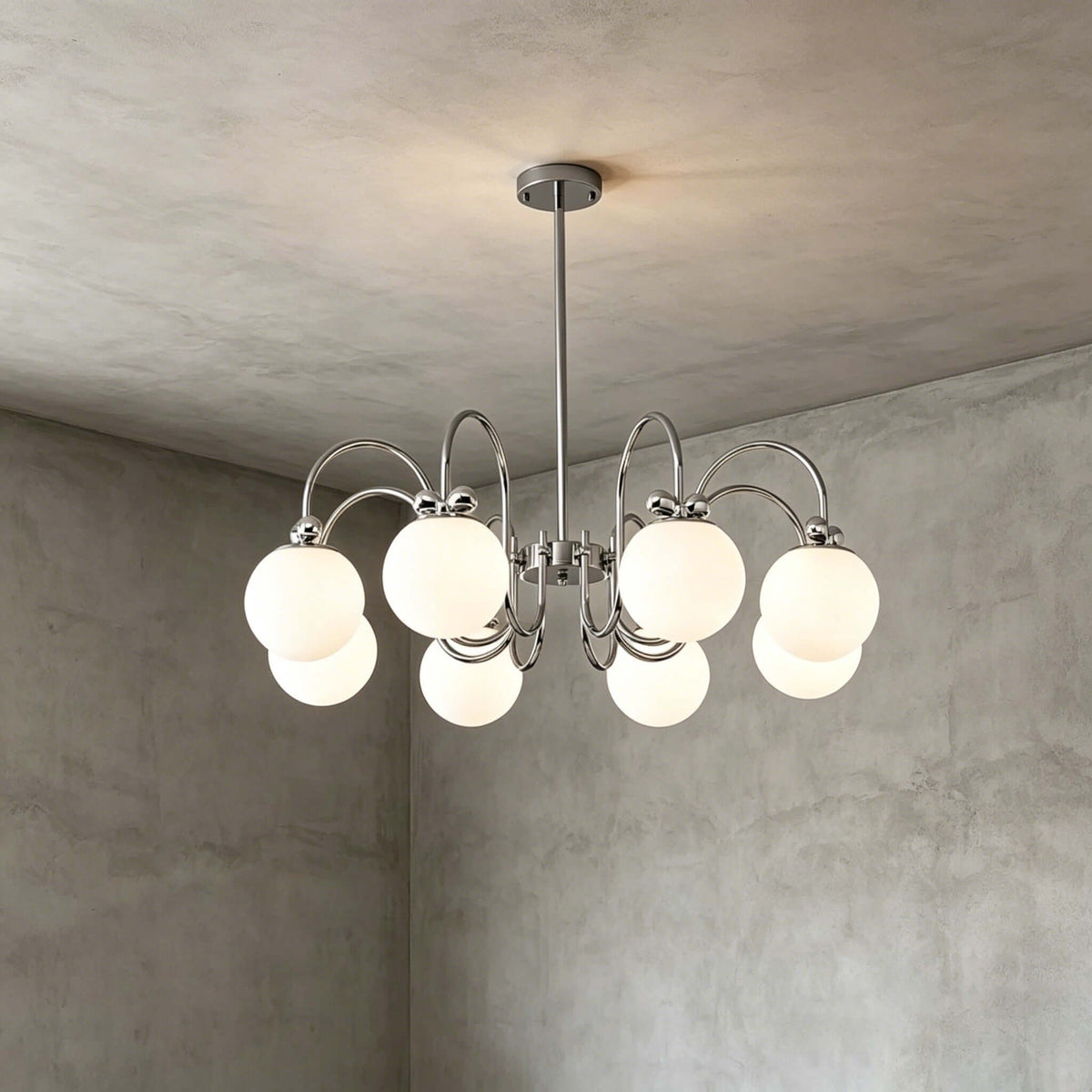 Closer view of the eight-globe version of this Clérachic chandelier, its chrome arms and white globes against a grey plaster corner.
