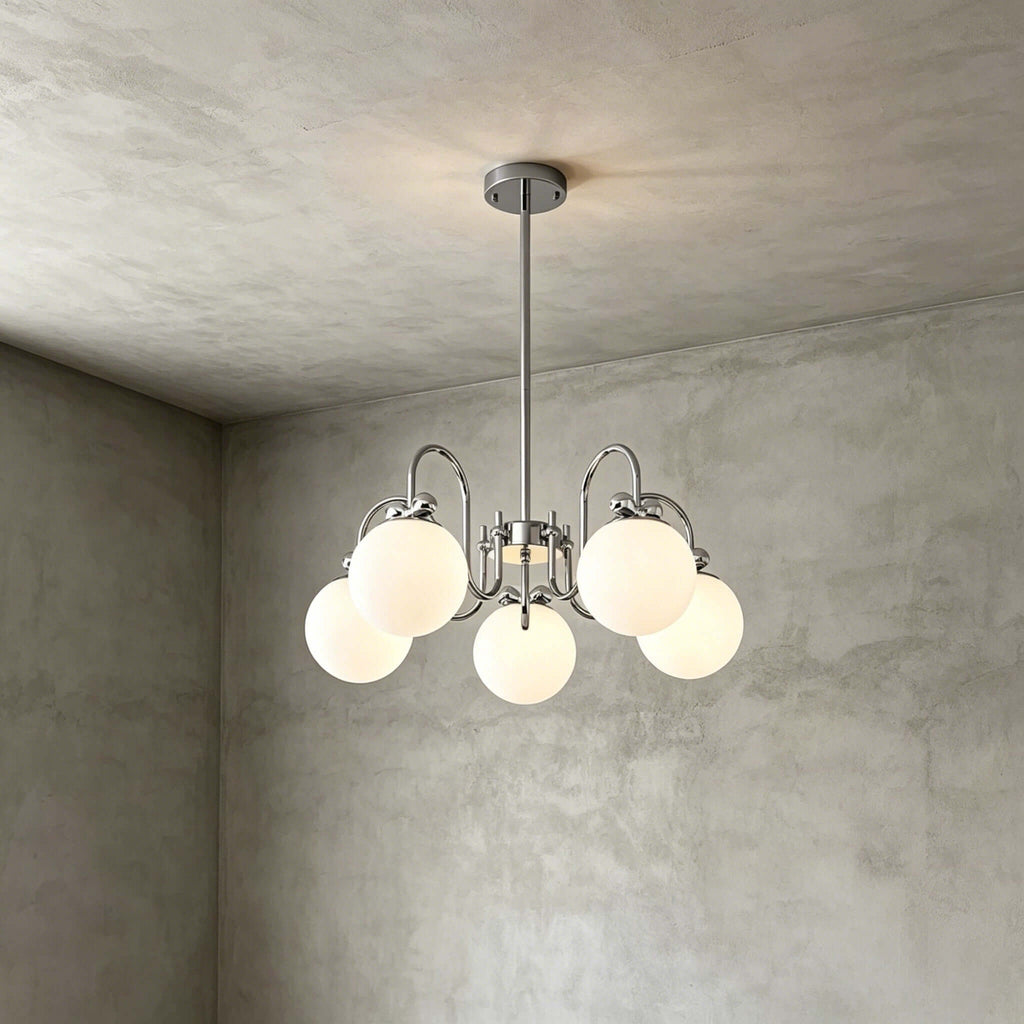 The five-globe version of this Clérachic chandelier hangs on a short rod against a grey plaster corner.