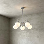 The five-globe version of this Clérachic chandelier hangs on a short rod against a grey plaster corner.
