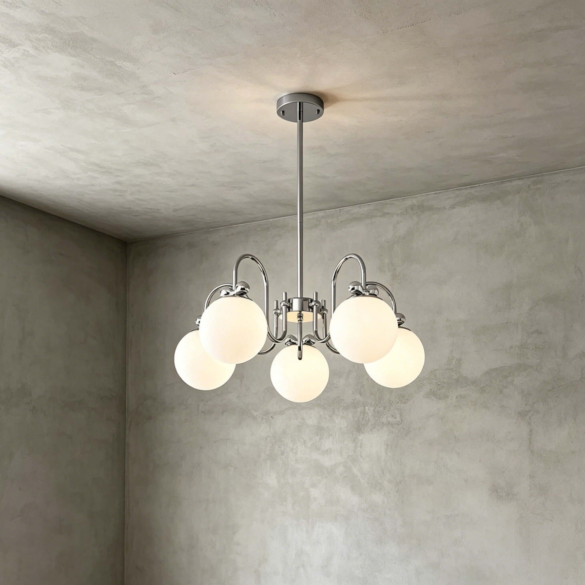 The five-globe version of this Clérachic chandelier hangs on a short rod against a grey plaster corner.