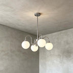 Four frosted globes on curving chrome arms, a Clérachic chandelier hung against a grey plaster wall.