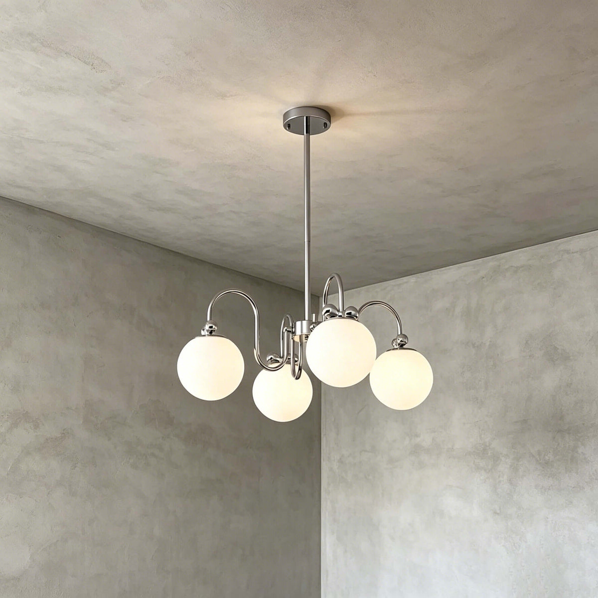 Four frosted globes on curving chrome arms, a Clérachic chandelier hung against a grey plaster wall.