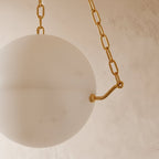 Close view of the Clérachic alabaster globe and a brass bracket with a chain link, showing soft cloudy veining