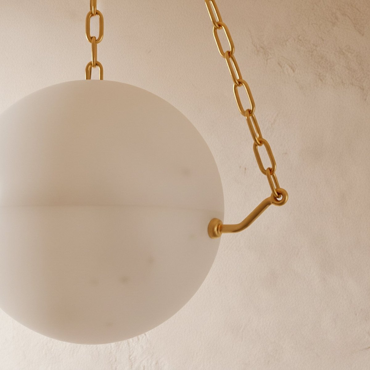 Close view of the Clérachic alabaster globe and a brass bracket with a chain link, showing soft cloudy veining