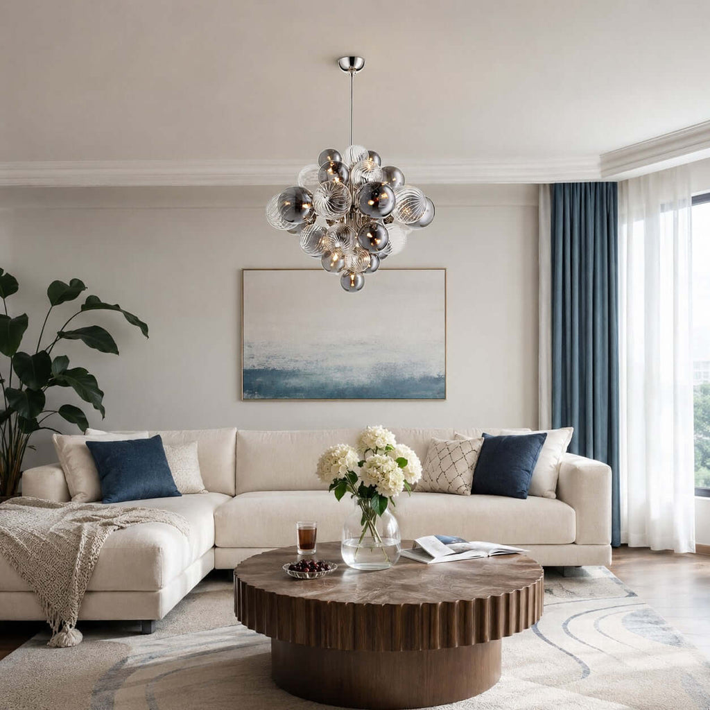 Clérachic glass-globe chandelier over a wooden drum coffee table, in a living room with blue curtains and a cream sofa.