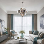 A Clérachic pendant of smoked and clear ribbed globes in a bright living room, with teal curtains behind a pale sofa.