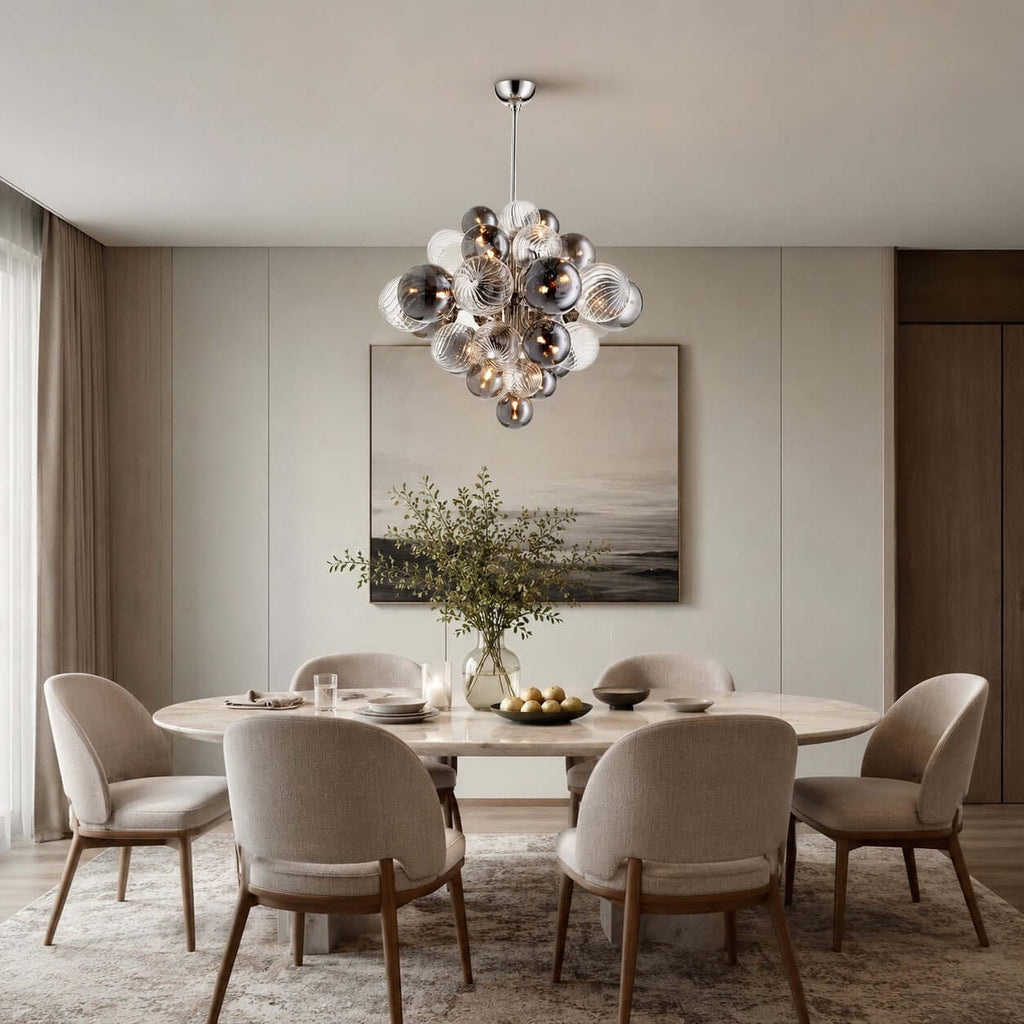 A Clérachic globe chandelier hangs over a round white dining table set with six upholstered chairs, in front of a landscape painting.