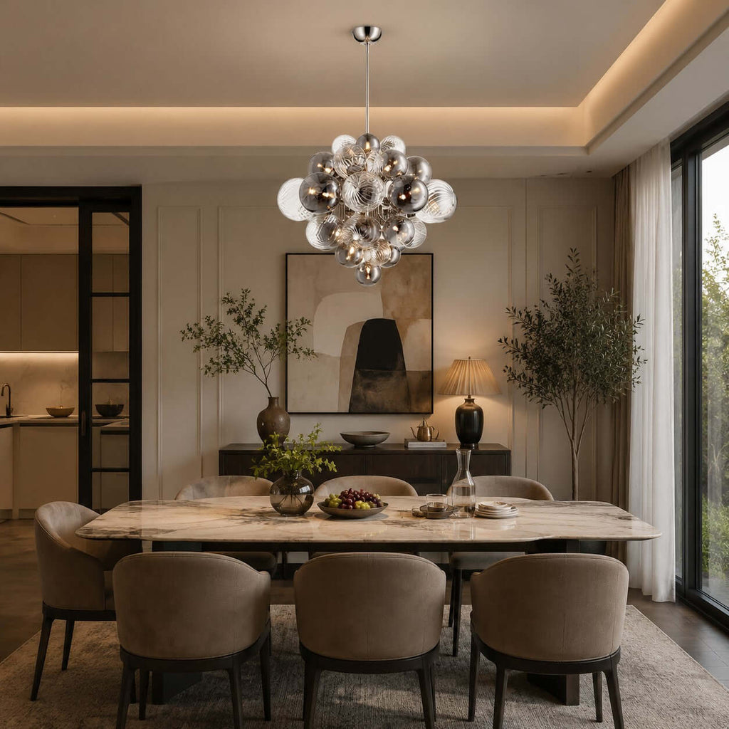 Lit Clérachic globe pendant above a marble-topped dining table with taupe chairs, under a ceiling with a warm cove light.