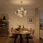 A Clérachic chandelier of ribbed glass globes glowing warm over a wooden dining table with cane chairs and a bowl of grapes.