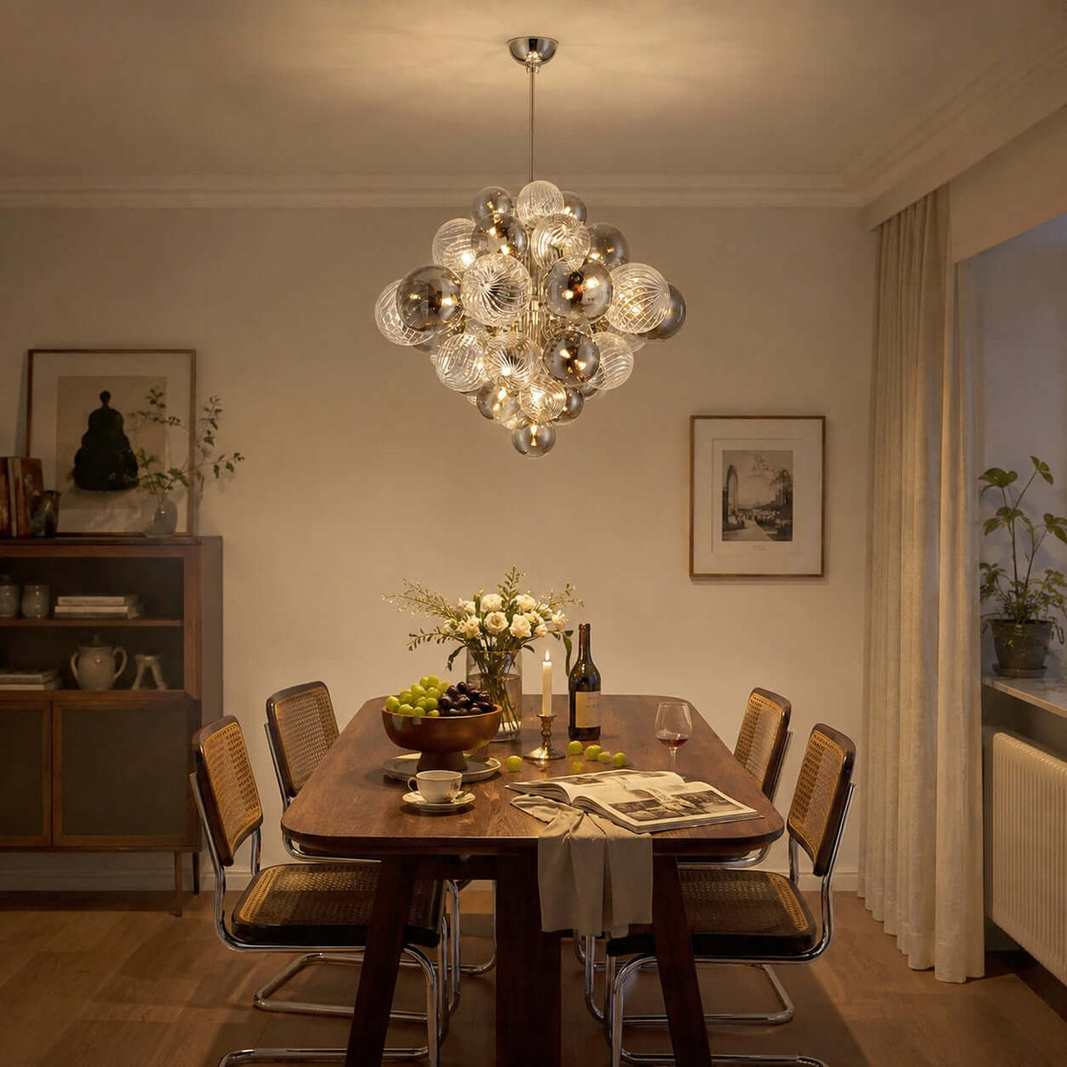 A Clérachic chandelier of ribbed glass globes glowing warm over a wooden dining table with cane chairs and a bowl of grapes.
