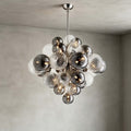 Close view of the Clérachic chandelier's smoked and swirl-ribbed glass globes around a chrome rod, with small lit bulbs inside.