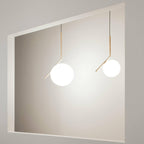 Two Clérachic globe pendants of different sizes hang from brass stems against a pale grey recessed wall, both glowing softly.
